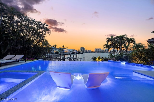 pool at dusk featuring a boat dock and a water view