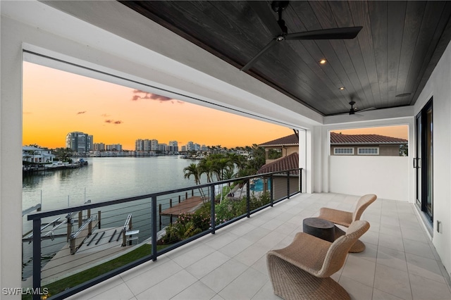 balcony at dusk featuring a water view and ceiling fan