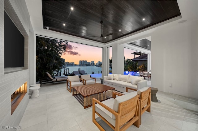 patio terrace at dusk featuring ceiling fan and an outdoor living space with a fireplace