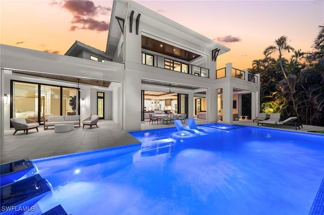 back house at dusk with pool water feature, a balcony, an outdoor living space, and a patio