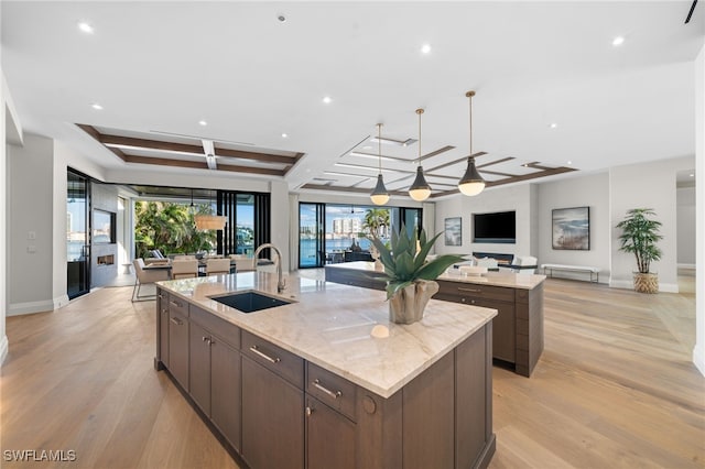 kitchen with a spacious island, dark brown cabinetry, coffered ceiling, sink, and light stone countertops