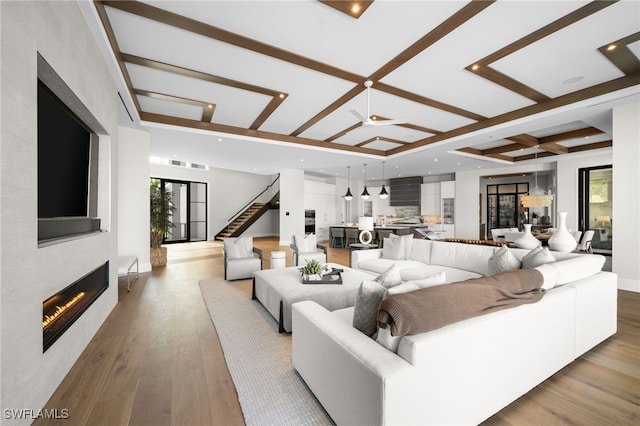 living room with coffered ceiling, light hardwood / wood-style flooring, a large fireplace, ceiling fan, and beam ceiling