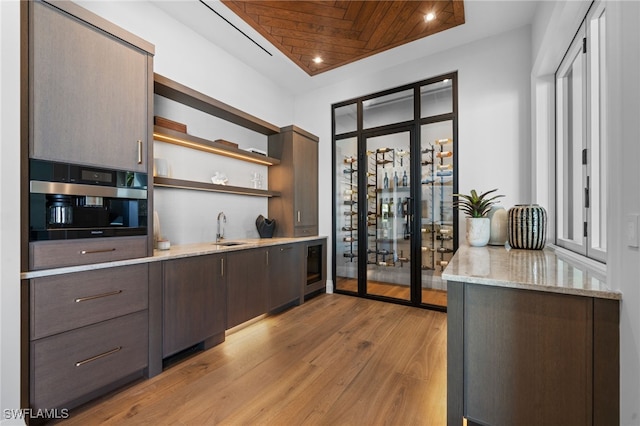 kitchen with sink, dark brown cabinets, light stone counters, oven, and light wood-type flooring