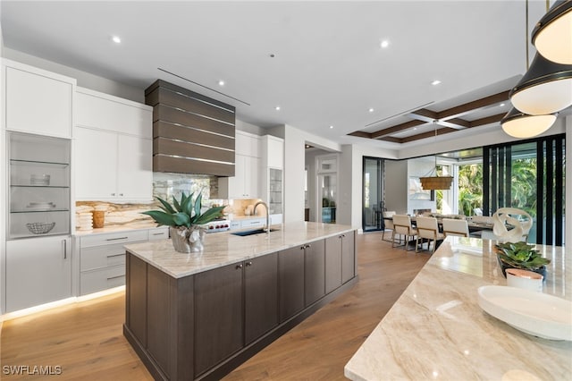 kitchen with coffered ceiling, a kitchen island with sink, sink, and white cabinets