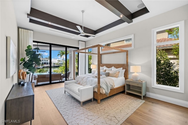 bedroom featuring a water view, access to exterior, light hardwood / wood-style flooring, and beamed ceiling