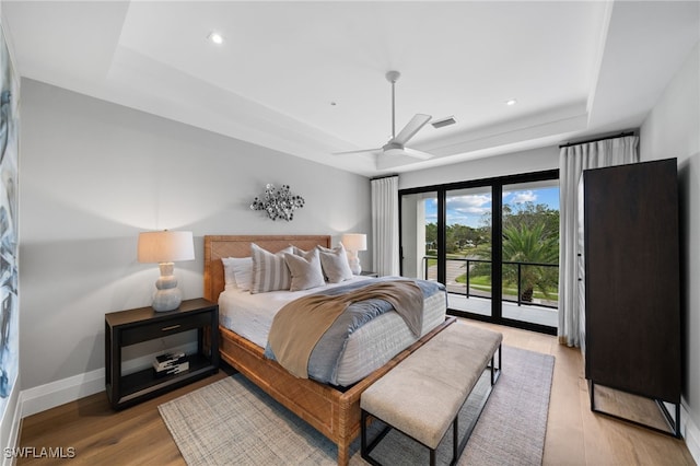 bedroom featuring light hardwood / wood-style flooring, a tray ceiling, access to outside, and ceiling fan