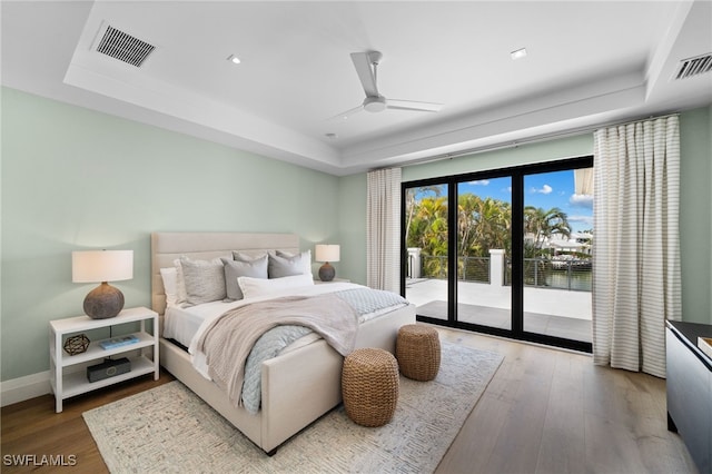 bedroom with ceiling fan, wood-type flooring, a tray ceiling, and access to exterior