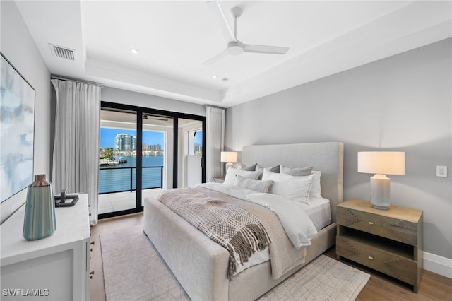 bedroom with light hardwood / wood-style flooring, access to exterior, ceiling fan, and a tray ceiling