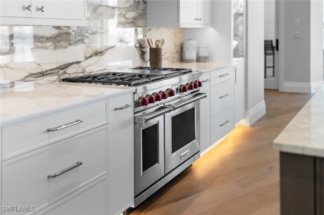 kitchen featuring light stone counters, double oven range, light hardwood / wood-style flooring, and white cabinets