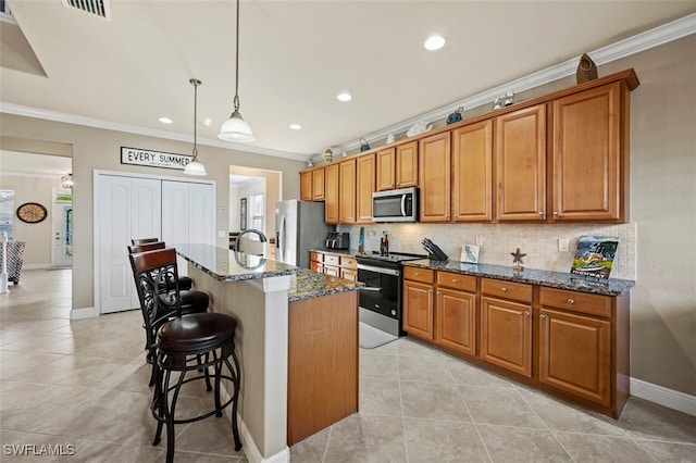 kitchen with a breakfast bar area, hanging light fixtures, a center island with sink, appliances with stainless steel finishes, and dark stone counters