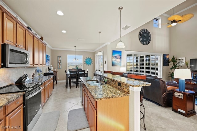 kitchen with sink, decorative light fixtures, appliances with stainless steel finishes, a kitchen breakfast bar, and a kitchen island with sink