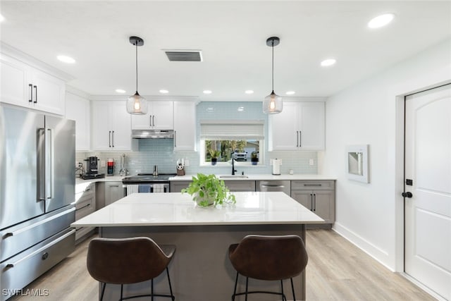 kitchen with white cabinetry, stainless steel appliances, a center island, and decorative light fixtures