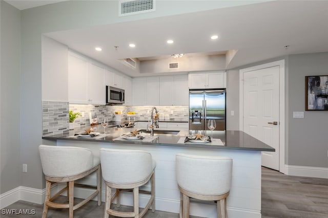 kitchen featuring sink, stainless steel appliances, tasteful backsplash, white cabinets, and kitchen peninsula