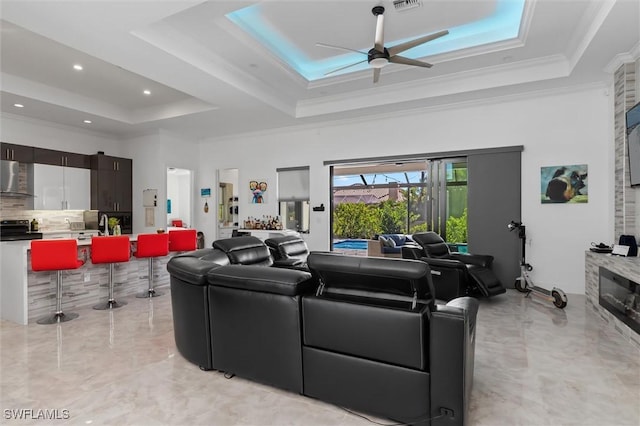 living room with ceiling fan, ornamental molding, a raised ceiling, and a high ceiling