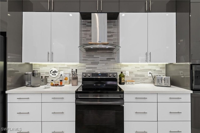 kitchen featuring wall chimney range hood, white cabinetry, black electric range, decorative backsplash, and built in fridge