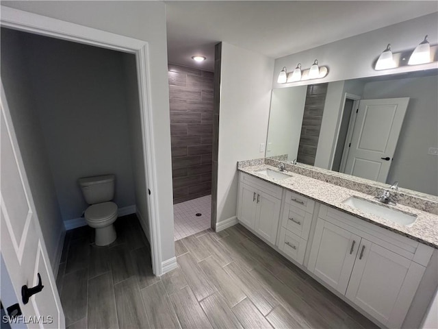 full bathroom with double vanity, tiled shower, baseboards, and a sink