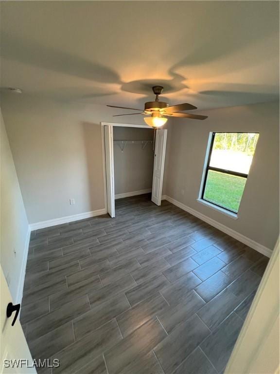 unfurnished bedroom with wood finish floors, a closet, baseboards, and a ceiling fan