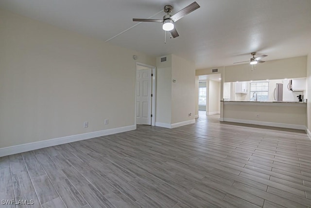 unfurnished living room with visible vents, baseboards, light wood-style flooring, ceiling fan, and a sink