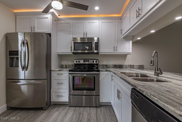 kitchen with light stone counters, a sink, a ceiling fan, white cabinets, and appliances with stainless steel finishes