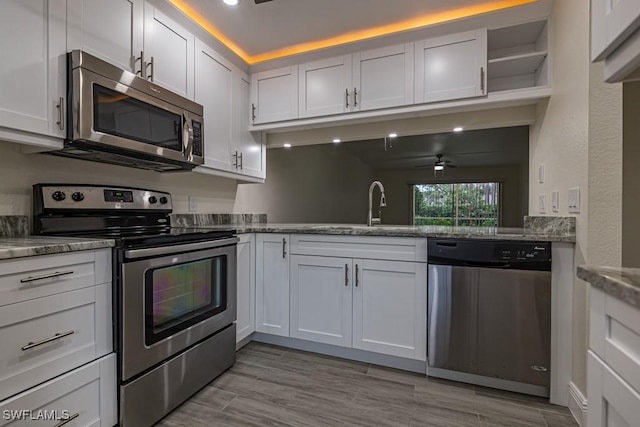 kitchen featuring sink, ceiling fan, appliances with stainless steel finishes, light stone countertops, and white cabinets