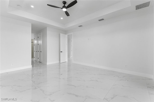 empty room with ceiling fan and a tray ceiling