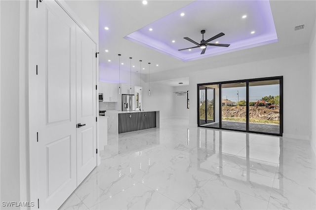 unfurnished living room featuring a raised ceiling and ceiling fan