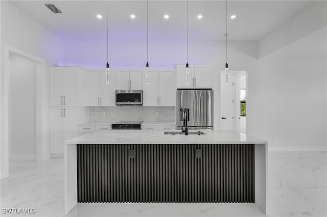 kitchen with stainless steel appliances, white cabinetry, a large island with sink, and decorative light fixtures