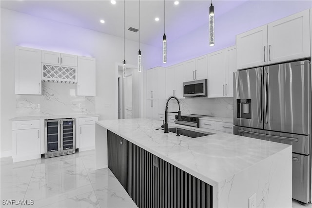 kitchen featuring hanging light fixtures, stainless steel appliances, wine cooler, an island with sink, and white cabinets