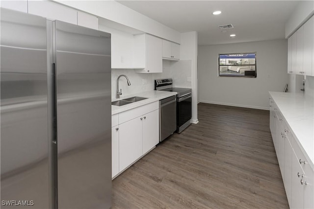 kitchen featuring appliances with stainless steel finishes, white cabinetry, sink, decorative backsplash, and light hardwood / wood-style flooring