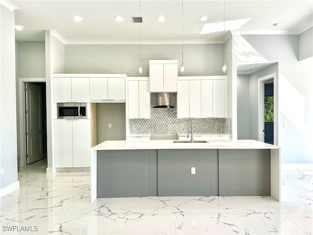 kitchen featuring white cabinetry, decorative light fixtures, wall chimney exhaust hood, and a center island with sink