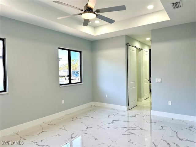 spare room with ceiling fan, a barn door, and a raised ceiling