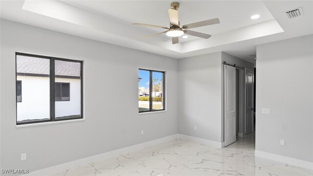 spare room featuring a barn door, baseboards, visible vents, marble finish floor, and a tray ceiling