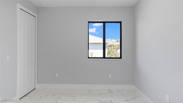 unfurnished bedroom featuring marble finish floor, baseboards, and a closet