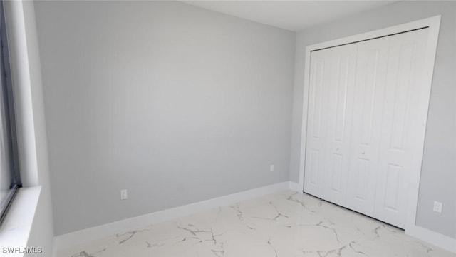 unfurnished bedroom with a closet, marble finish floor, and baseboards