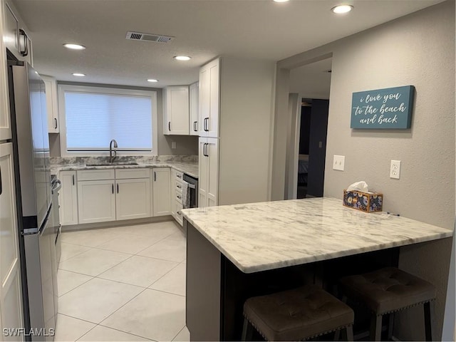 kitchen featuring stainless steel fridge, light stone countertops, sink, and white cabinets