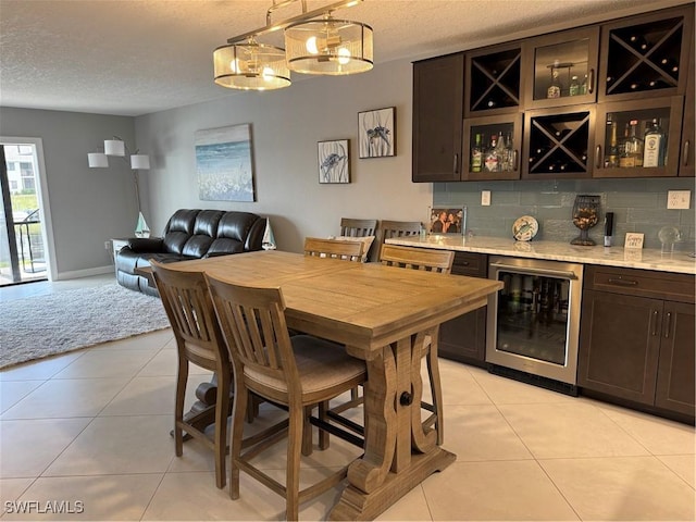 dining space featuring wine cooler, bar area, a textured ceiling, and light tile patterned flooring