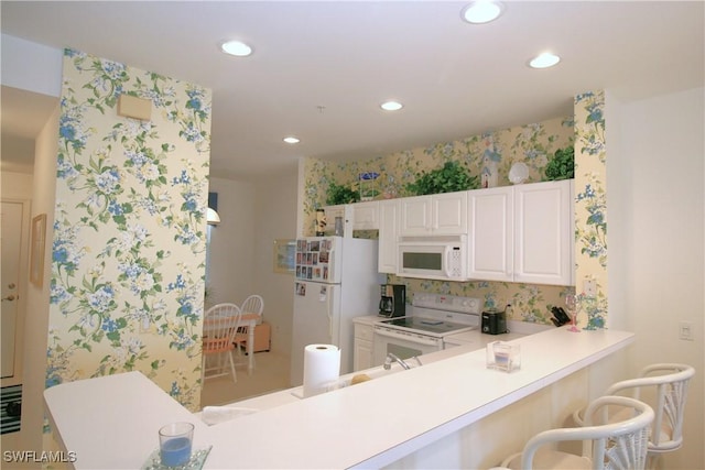 kitchen featuring white cabinetry, white appliances, a breakfast bar, and kitchen peninsula