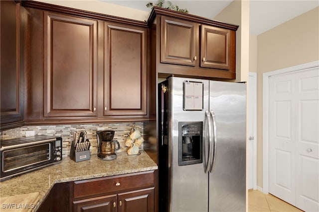 kitchen with light tile patterned flooring, dark brown cabinets, stainless steel fridge, light stone countertops, and backsplash