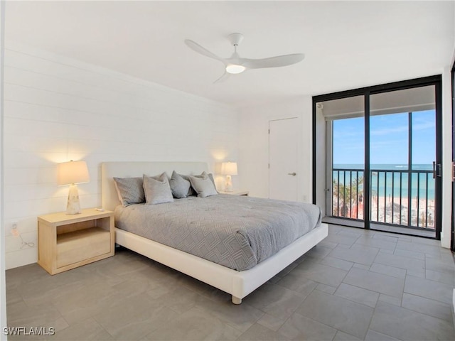 bedroom featuring access to outside, expansive windows, ceiling fan, and a water view