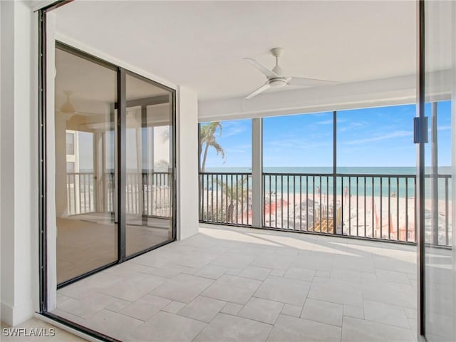 unfurnished sunroom with a view of the beach, ceiling fan, and a water view