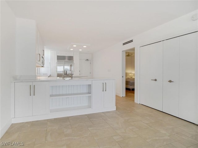 interior space featuring built in refrigerator, white cabinetry, sink, and kitchen peninsula