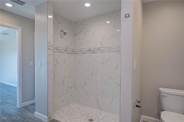 bathroom with wood-type flooring, toilet, and a tile shower