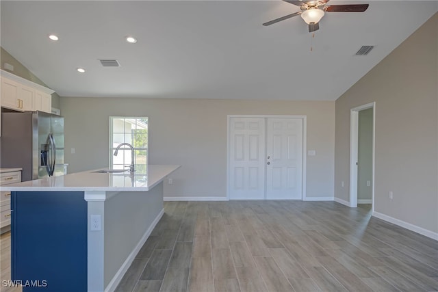 kitchen with lofted ceiling, sink, white cabinets, stainless steel fridge, and a kitchen island with sink