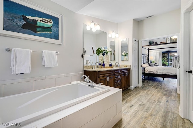 bathroom featuring wood-type flooring, vanity, and tiled tub