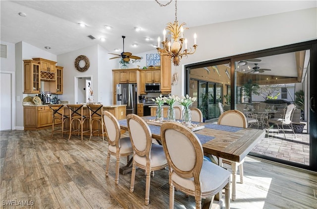 dining area featuring ceiling fan with notable chandelier, vaulted ceiling, and light hardwood / wood-style flooring