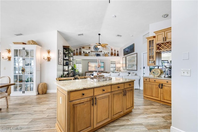 kitchen with light stone countertops, vaulted ceiling, a kitchen island, and ceiling fan