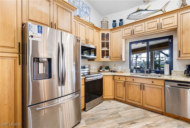 kitchen with stainless steel appliances, sink, light stone counters, and light wood-type flooring