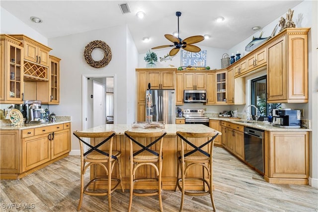 kitchen with sink, light stone counters, vaulted ceiling, a kitchen island, and stainless steel appliances