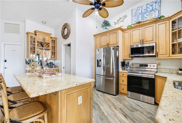 kitchen with a kitchen bar, light stone counters, light hardwood / wood-style flooring, ceiling fan, and stainless steel appliances