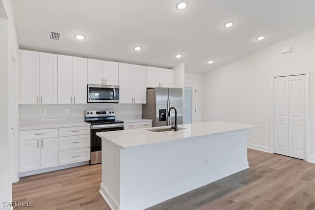 kitchen with light hardwood / wood-style flooring, stainless steel appliances, white cabinets, and a center island with sink